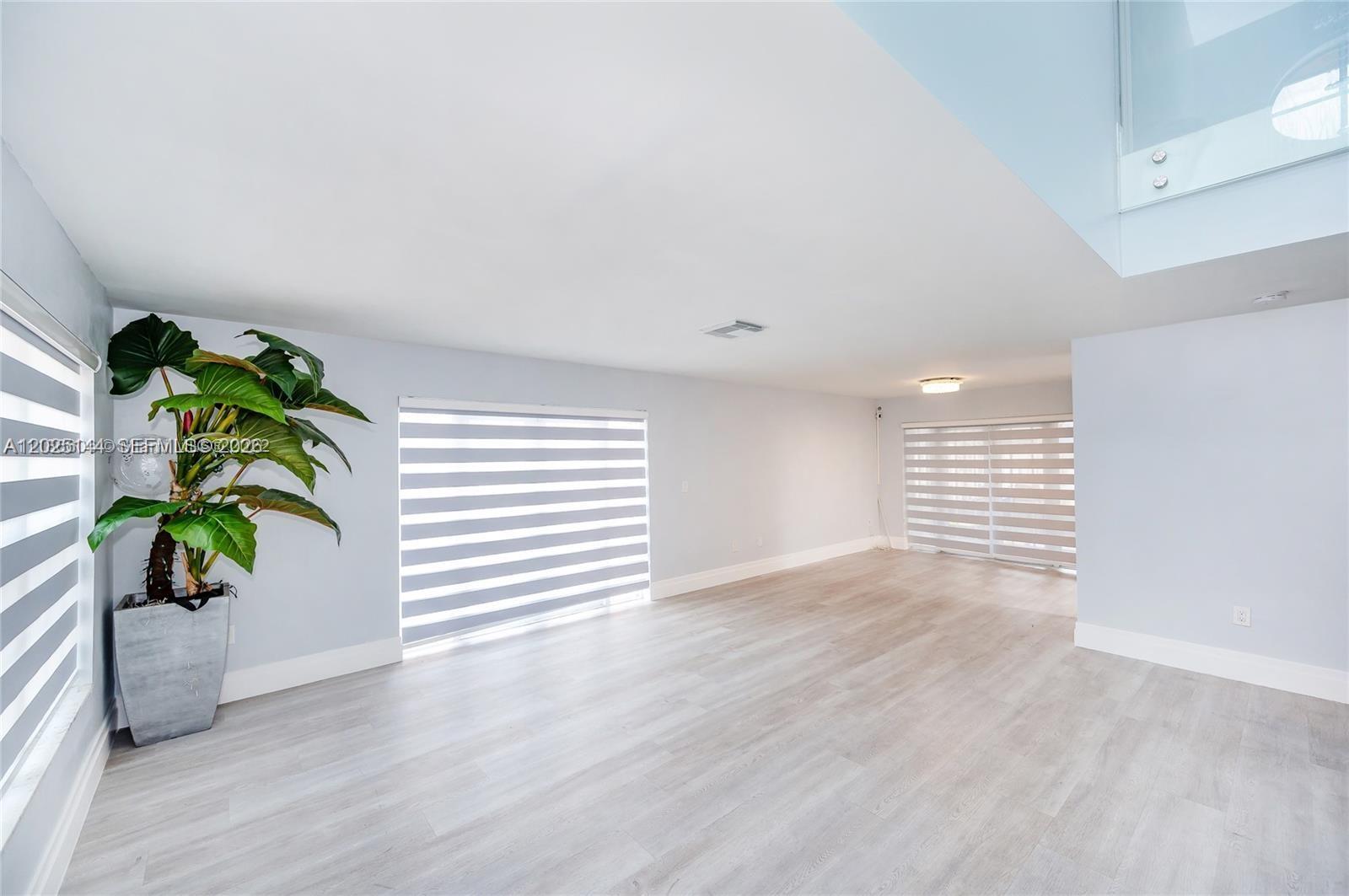 A bright, empty room features light wood-look flooring, pale walls, and modern striped window shades — 18660 NW 78th Ave # 0, Hialeah FL 33015, HIALEAH, FL