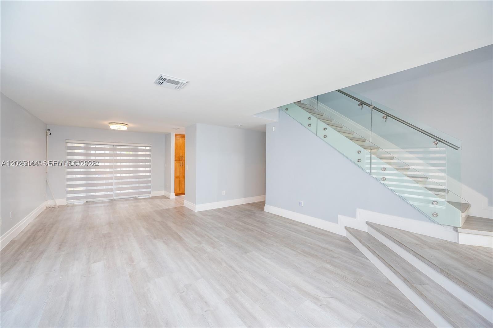 An open living area features light-colored wood flooring, a glass-railed staircase, and large windows — 18660 NW 78th Ave # 0, Hialeah FL 33015, HIALEAH, FL