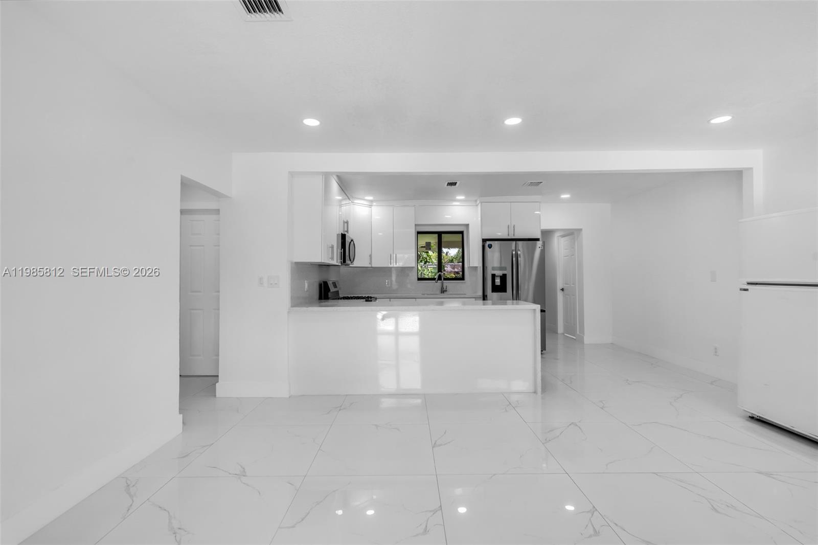A modern kitchen features white cabinetry, a breakfast bar, and white marble-patterned tile flooring — 1010 NE 140th St, North Miami FL 33161, NORTH MIAMI, FL