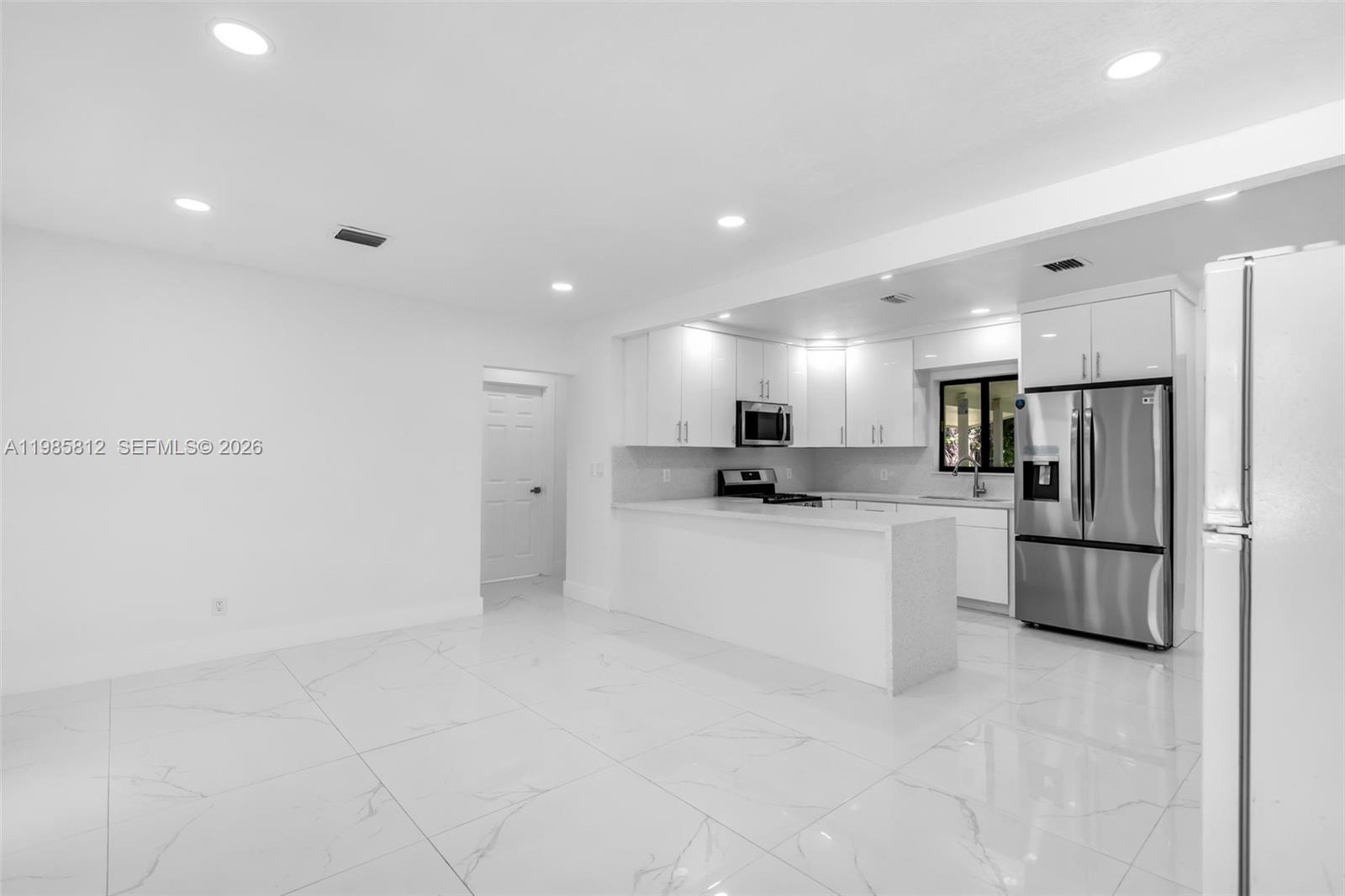 This kitchen features white cabinets, stainless steel appliances, and light-colored tile flooring — 1010 NE 140th St, North Miami FL 33161, NORTH MIAMI, FL