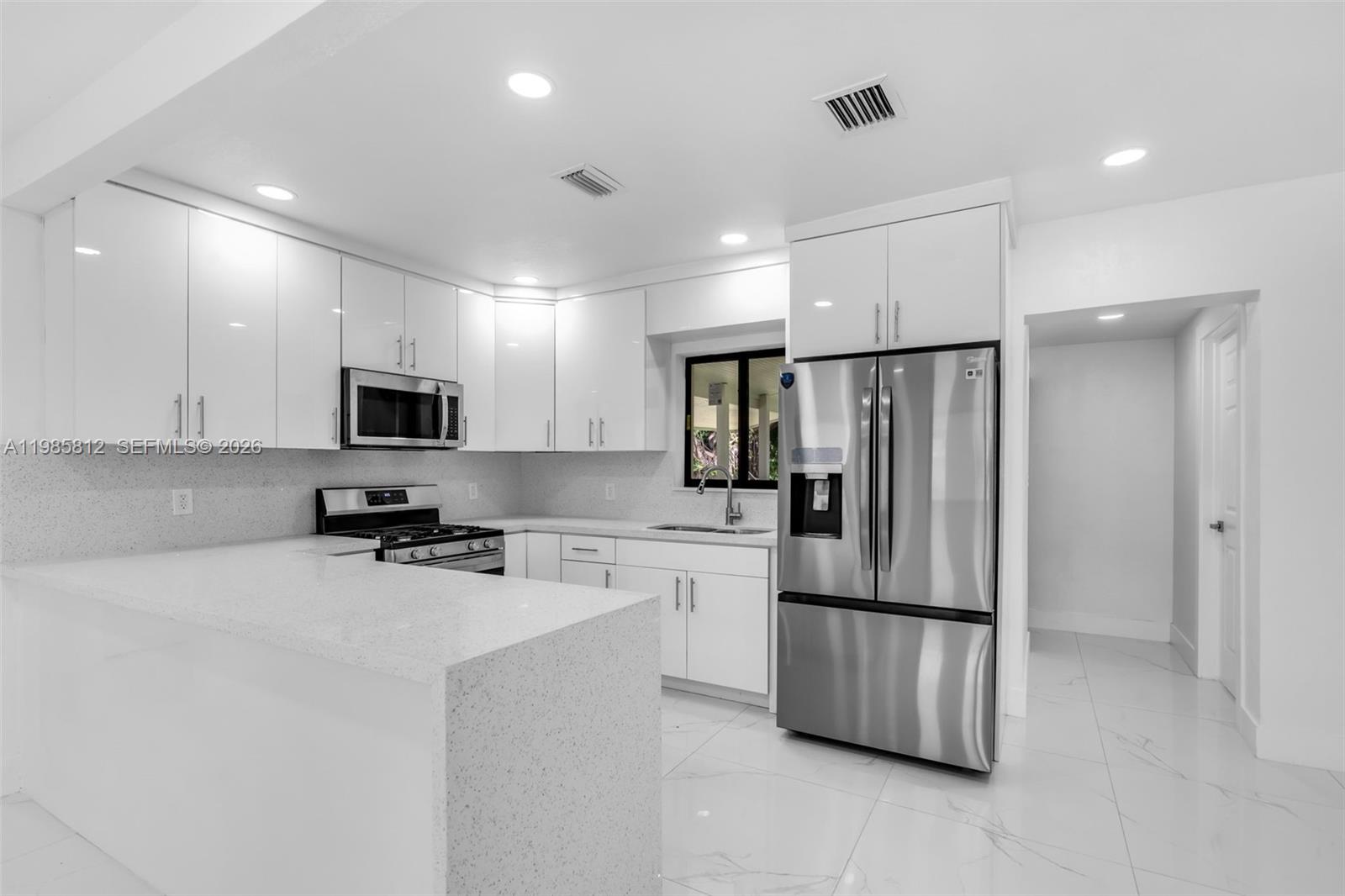 A modern kitchen features white cabinets, stainless steel appliances, and white quartz countertops — 1010 NE 140th St, North Miami FL 33161, NORTH MIAMI, FL