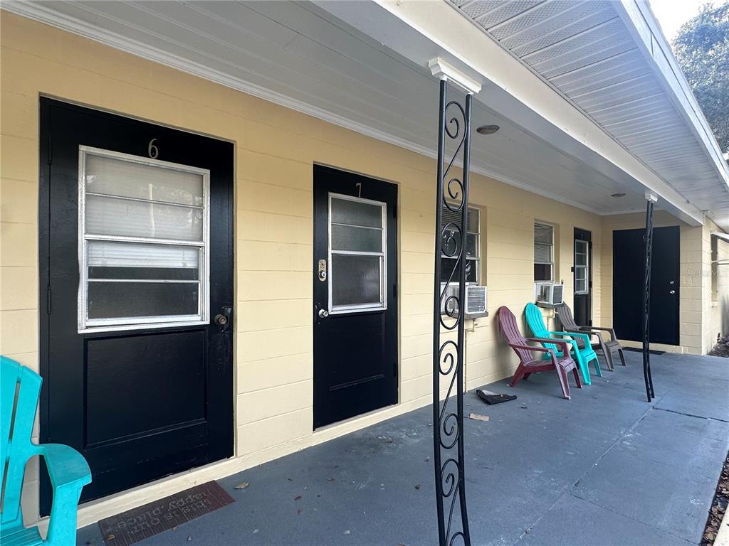 A row of apartment doors with black frames and matching chairs on a covered porch — 3618 N SCENIC HWY UNIT 2, LAKE WALES, FL