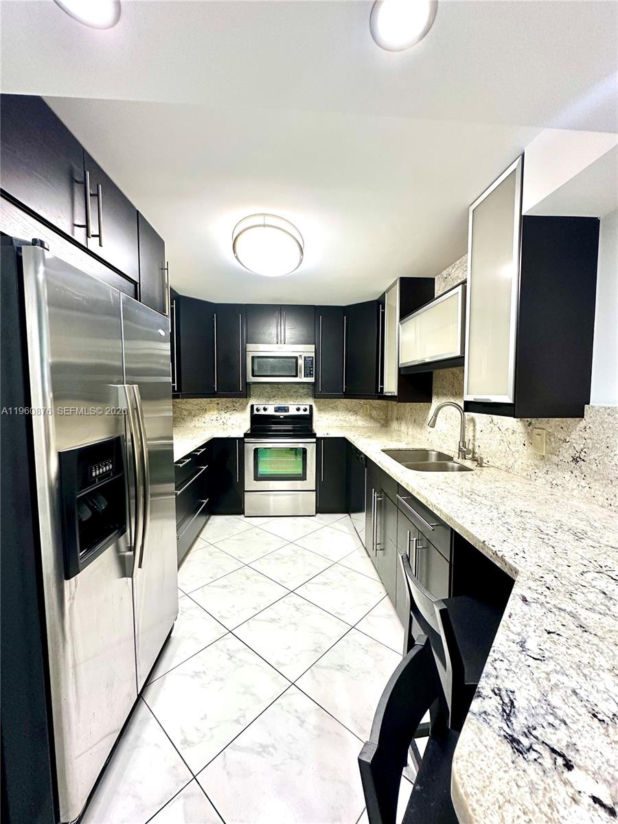 A galley kitchen features dark cabinetry, stainless steel appliances, and light granite countertops — 1904 S Ocean Dr # 701, Hallandale Beach FL 33009, HALLANDALE BEACH, FL