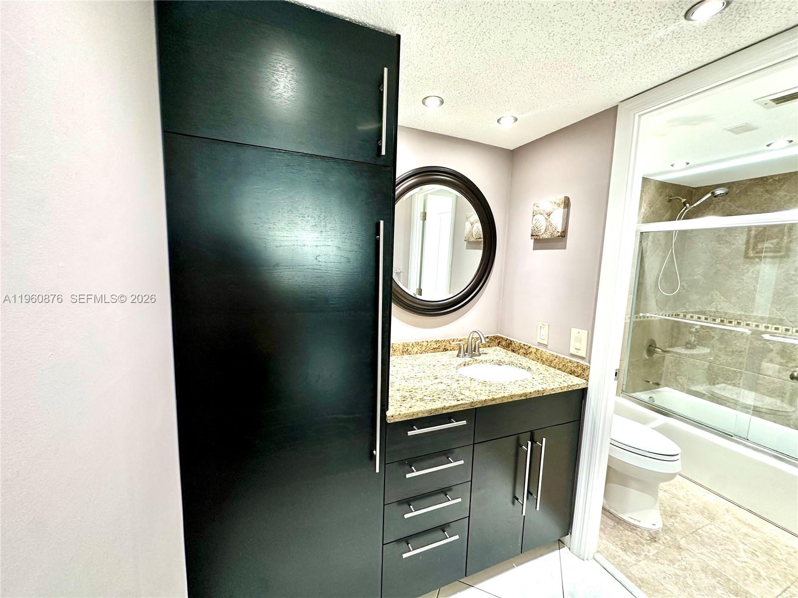 A bathroom features a dark wood vanity, granite countertop, round mirror, and a glass-enclosed shower — 1904 S Ocean Dr # 701, Hallandale Beach FL 33009, HALLANDALE BEACH, FL