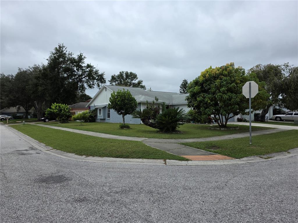 A single-story house with a light-colored exterior sits on a corner lot with landscaping — 13202 PINE CREEK CIRCLE, RIVERVIEW, FL