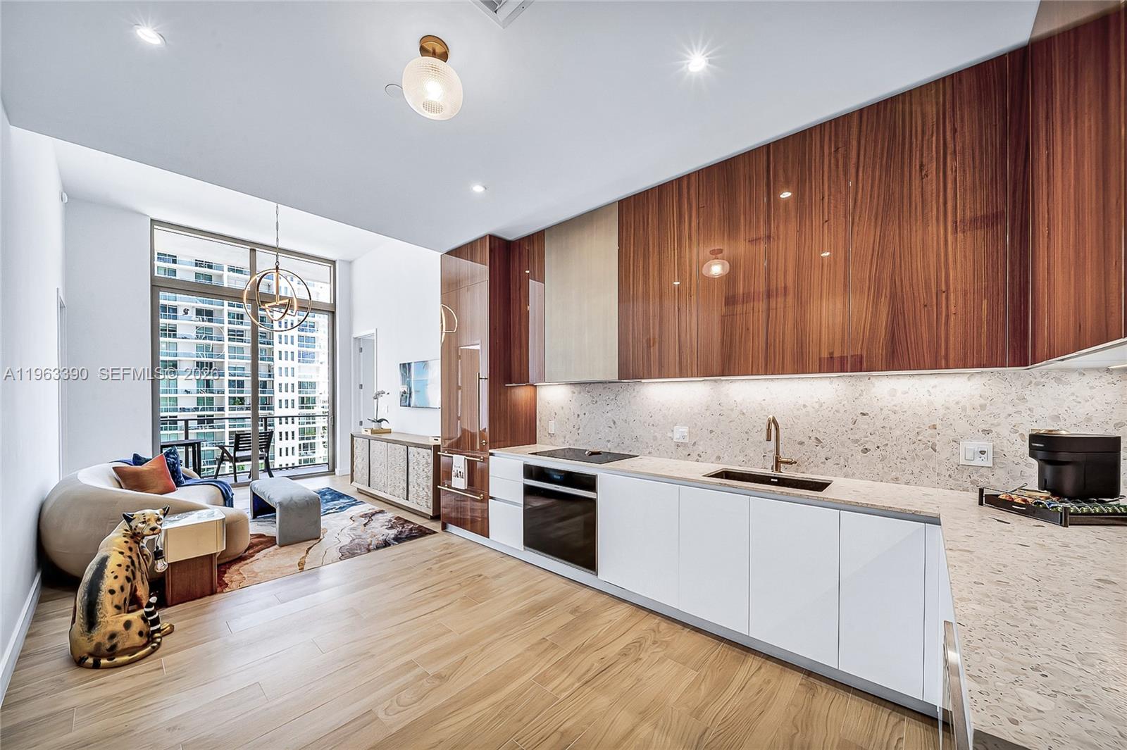 A modern kitchen with wood-veneer upper cabinets and white lower cabinets opens to a living area — 2655 S Bayshore Dr # 706, Miami FL 33133, MIAMI, FL