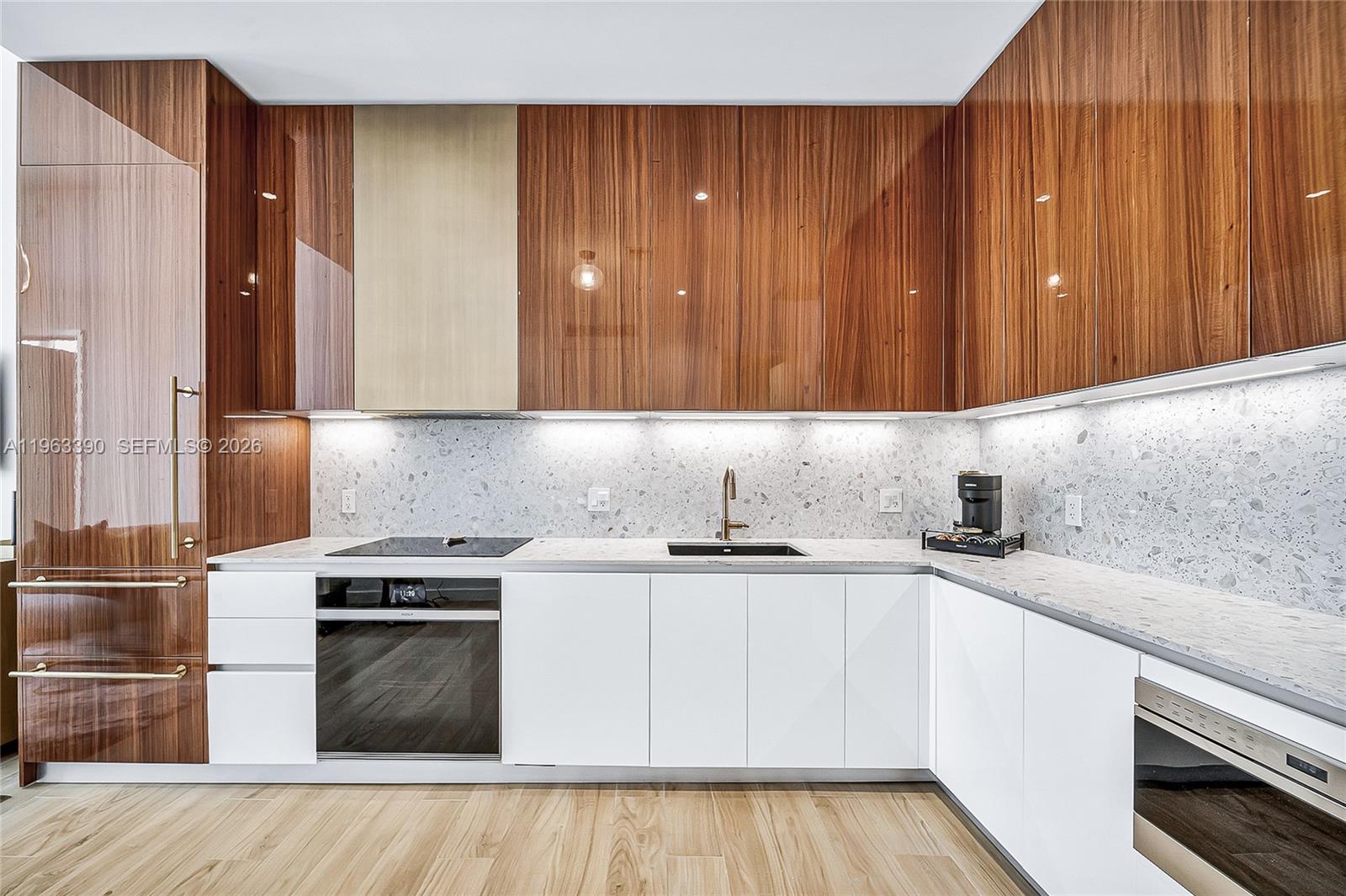 A modern kitchen features wood-veneer upper cabinets, white lower cabinets, and a speckled stone backsplash — 2655 S Bayshore Dr # 706, Miami FL 33133, MIAMI, FL