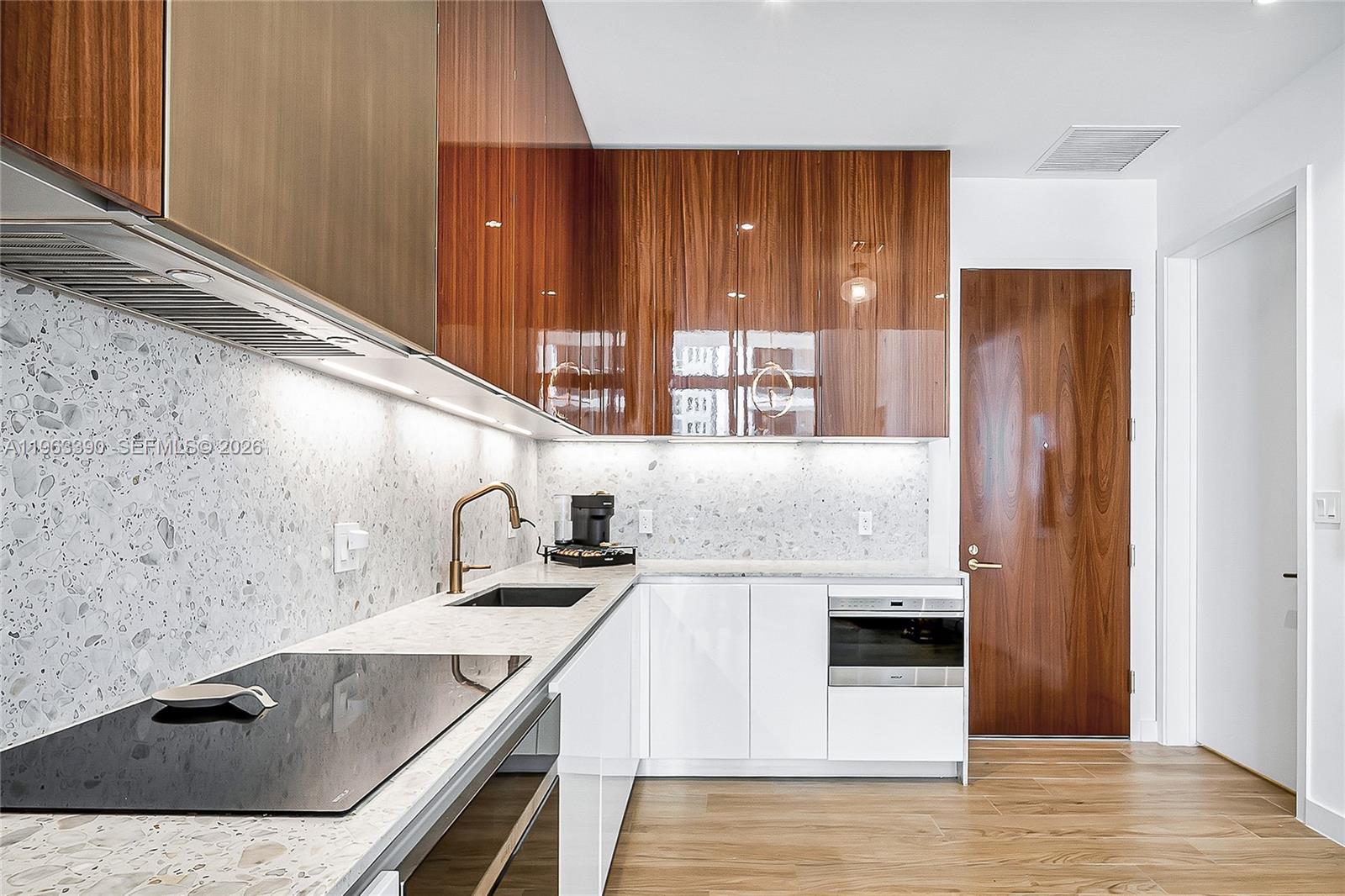 A modern kitchen features wood-veneer cabinets, white lower cabinets, and a speckled stone backsplash — 2655 S Bayshore Dr # 706, Miami FL 33133, MIAMI, FL