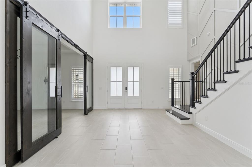 A bright foyer features white tile flooring, a staircase with black railings, and glass barn doors — 9652 ENGLISH LAUREL COURT, ORLANDO, FL