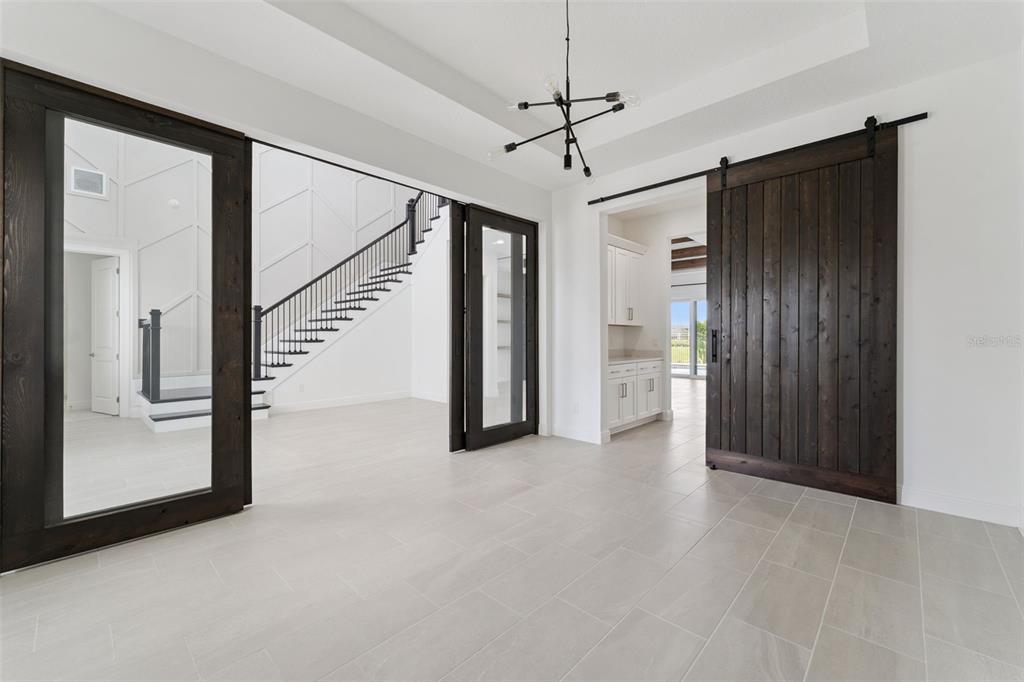 A bright room features large dark wood-framed glass doors, a sliding barn door, and tile flooring — 9652 ENGLISH LAUREL COURT, ORLANDO, FL