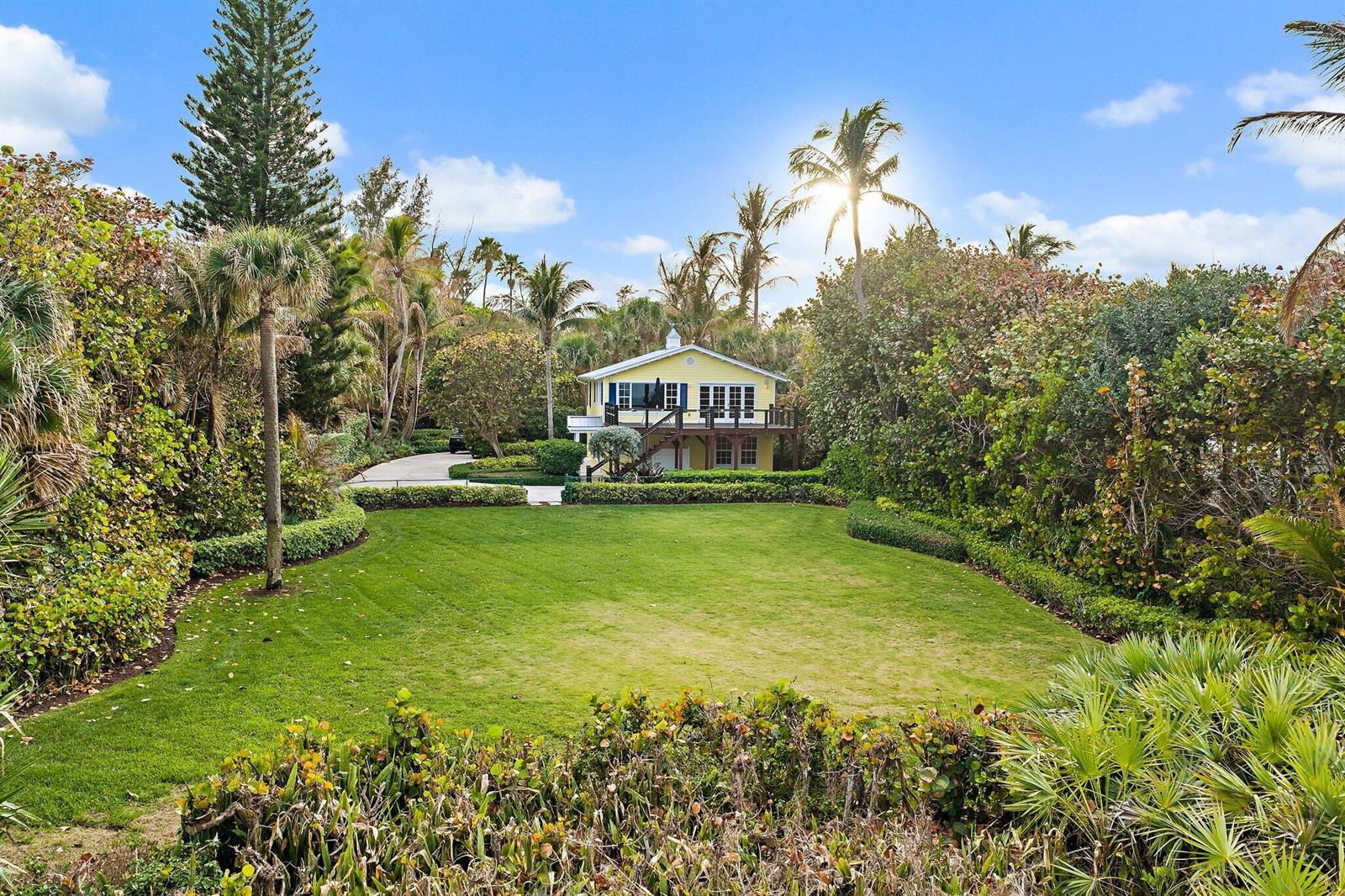 A yellow two-story house sits behind a large green lawn surrounded by lush tropical landscaping — 31 N Beach Road, Jupiter Island FL 33455, JUPITER ISLAND, FL