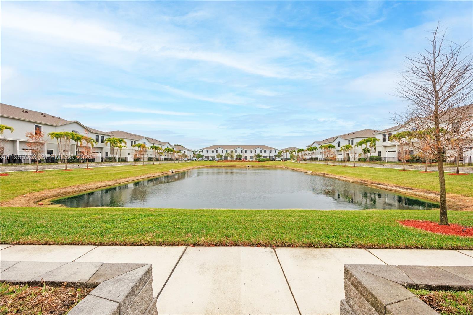 A pond sits between rows of two-story townhouses under a blue sky — 369 NW 8th Ct, Pompano Beach FL 33060, POMPANO BEACH, FL