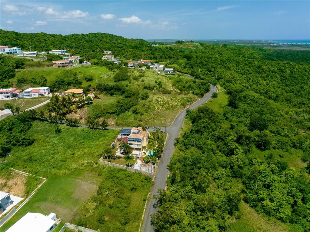 An aerial view shows a house with solar panels situated on a hillside near a road — Barrio Mameyes LINDO MAR II Lote 14, RIO GRANDE, PR