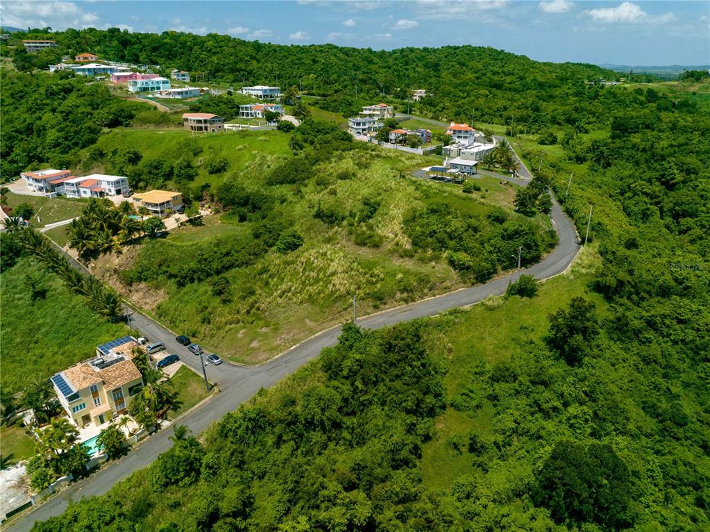 An aerial view shows a winding road passing through a hilly, green residential area — Barrio Mameyes LINDO MAR II Lote 14, RIO GRANDE, PR