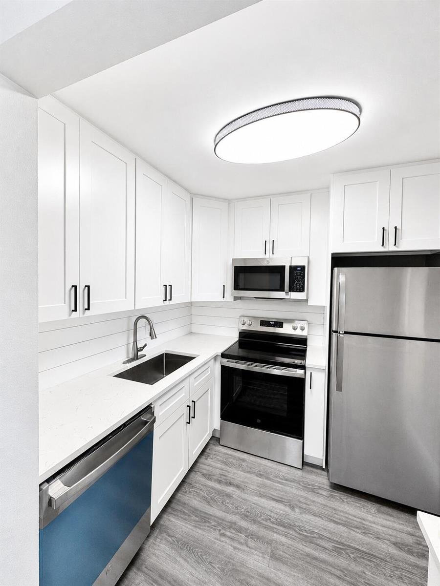 A modern kitchen features white cabinets, stainless steel appliances, and gray wood-look flooring — 115 S South Boulevard # 2c, Boynton Beach FL 33435, BOYNTON BEACH, FL