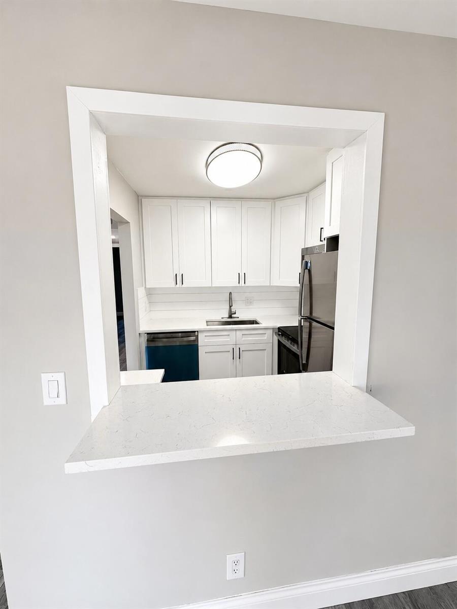 A kitchen pass-through window with a white quartz countertop overlooks a modern white kitchen — 115 S South Boulevard # 2c, Boynton Beach FL 33435, BOYNTON BEACH, FL