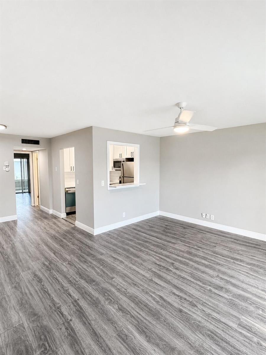An empty living room with gray wood-look flooring, a ceiling fan, and a kitchen pass-through — 115 S South Boulevard # 2c, Boynton Beach FL 33435, BOYNTON BEACH, FL