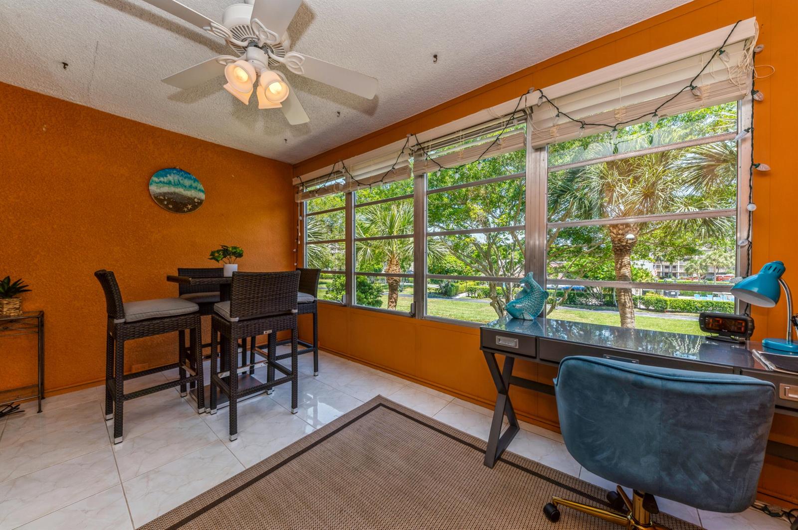 A sunroom with orange walls, a dining set, a desk, and large windows overlooking trees — 14527 Bonaire Boulevard # 303, Delray Beach FL 33446, DELRAY BEACH, FL