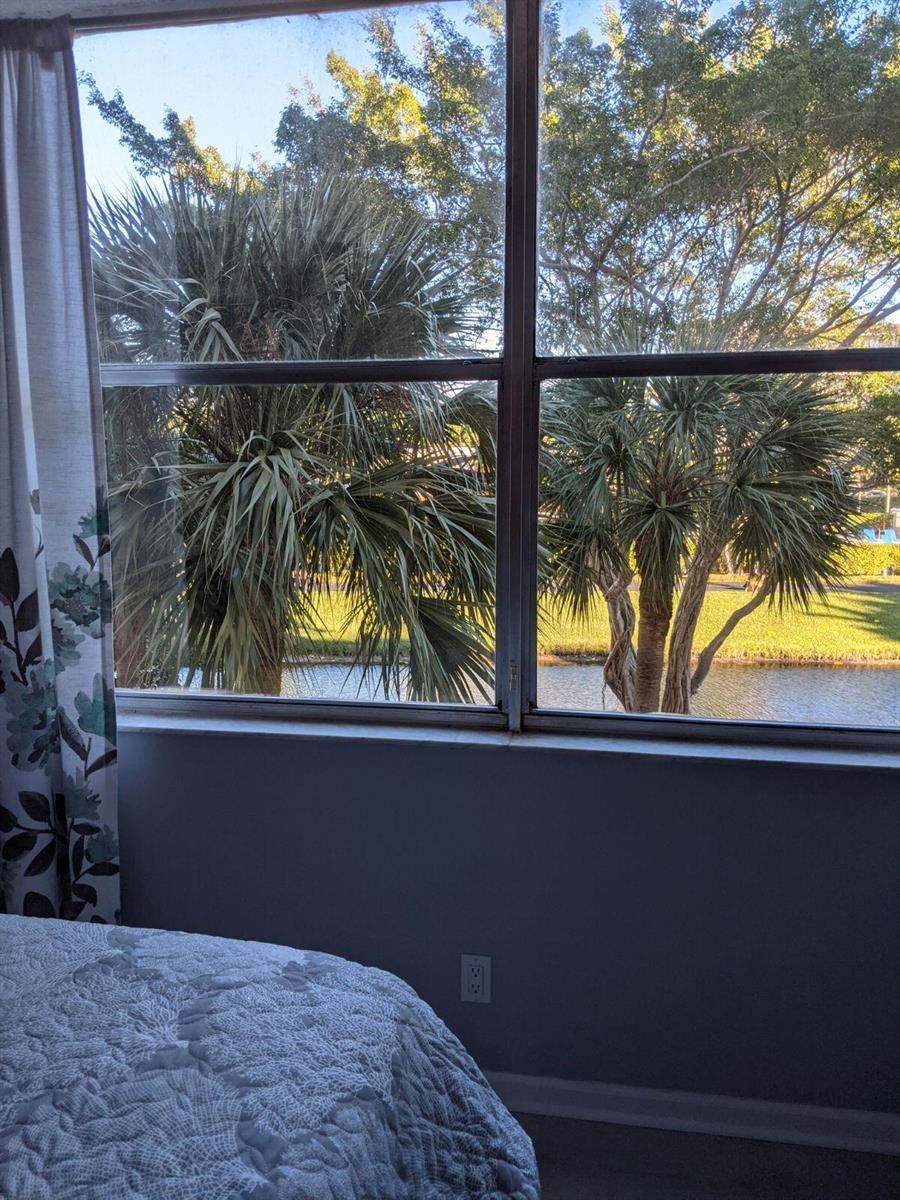 A bedroom window overlooks a canal and palm trees with a bed in the foreground — 14527 Bonaire Boulevard # 303, Delray Beach FL 33446, DELRAY BEACH, FL