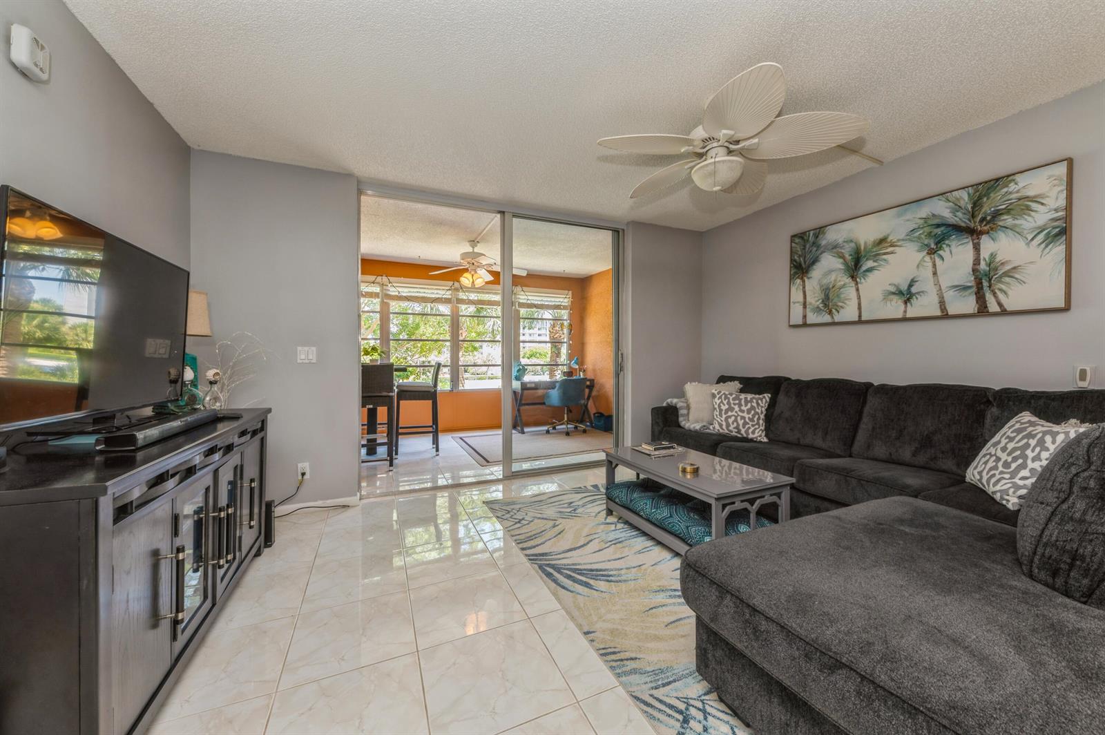 A living room with a dark sectional sofa, tile flooring, and a sliding door to a balcony — 14527 Bonaire Boulevard # 303, Delray Beach FL 33446, DELRAY BEACH, FL