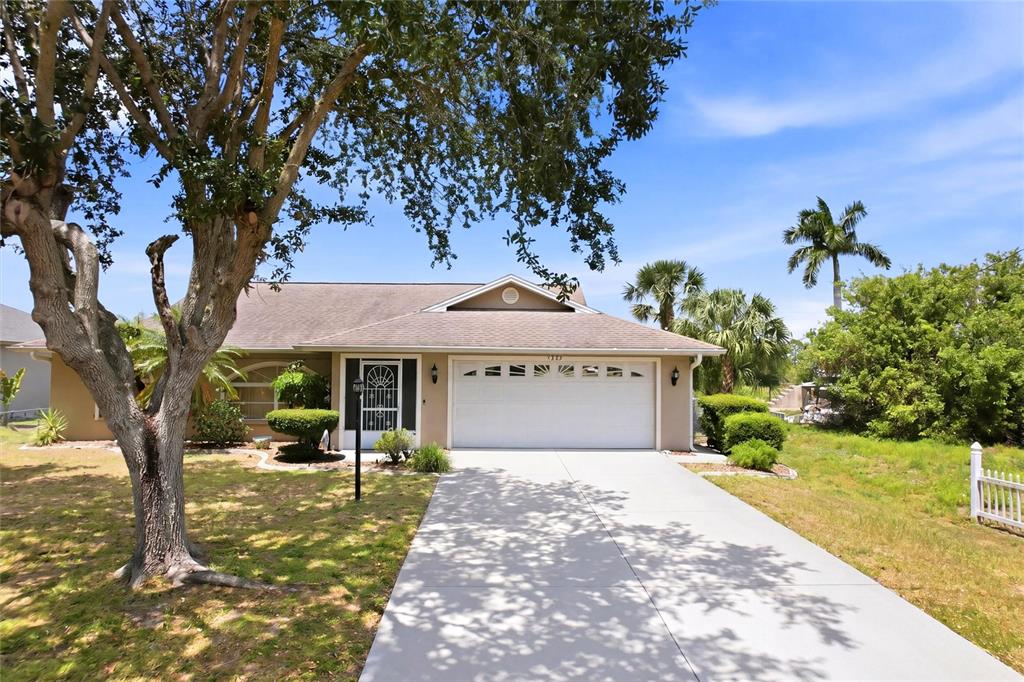 A single-story house with a white garage door, a concrete driveway, and a large tree — 1299 TRIPOLI STREET, NORTH PORT, FL