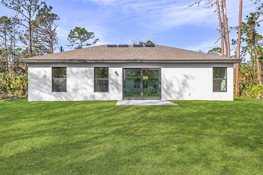 The rear exterior of a single-story white stucco house features a sliding glass door — 3453 WORTHINGTON AVENUE, NORTH PORT, FL