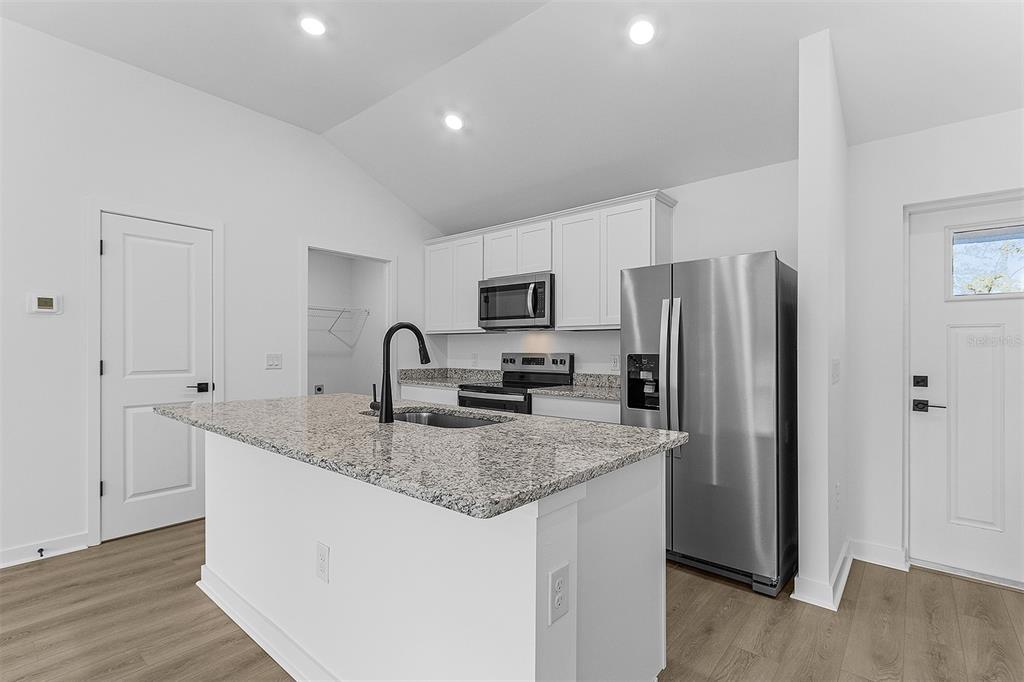 A modern kitchen features white cabinets, granite countertops, a center island, and stainless steel appliances — 3453 WORTHINGTON AVENUE, NORTH PORT, FL