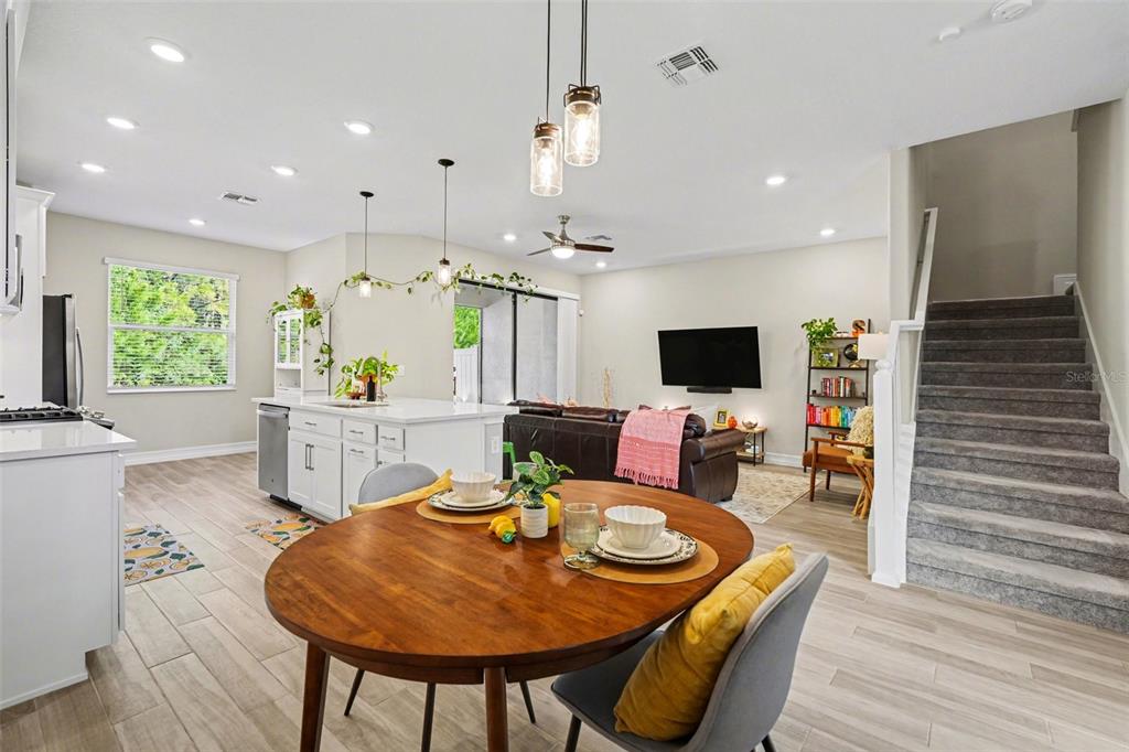 An open-concept kitchen and dining area features white cabinetry, a wooden table, and carpeted stairs — 5054 SAN MARTINO DRIVE, WESLEY CHAPEL, FL
