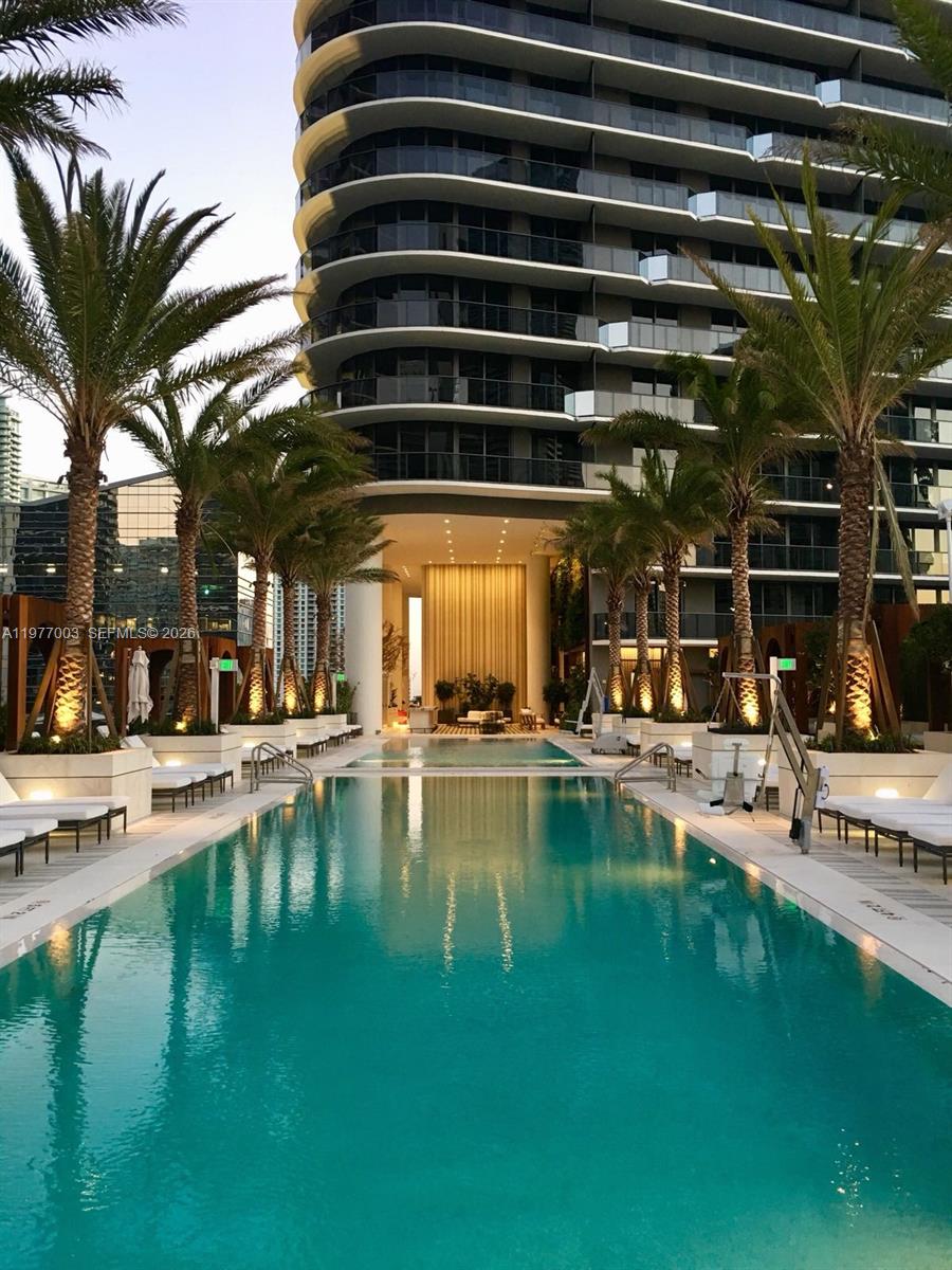 A long swimming pool is centered between rows of palm trees and a modern building — 801 S Miami Ave # 1705, Miami FL 33131, MIAMI, FL