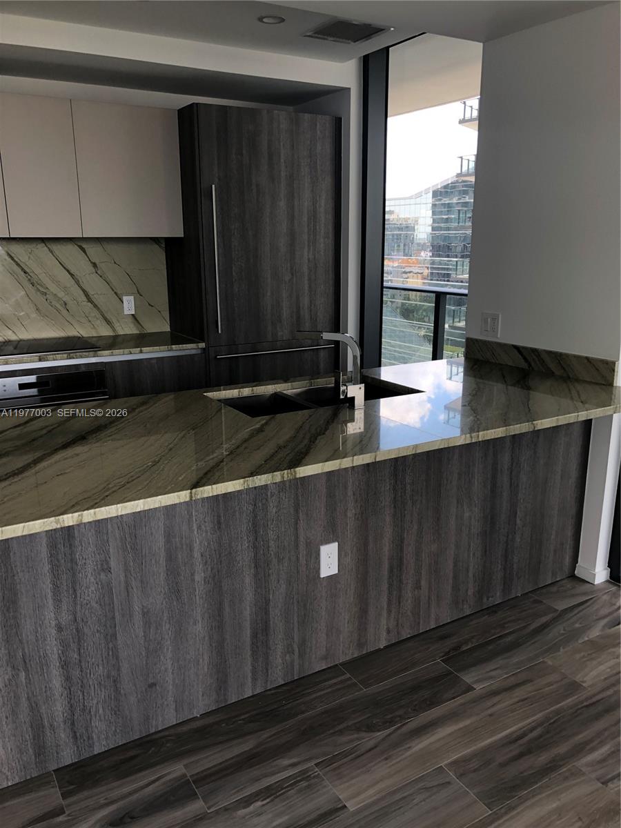 A modern kitchen features dark wood cabinetry, stone countertops, and a view of city buildings — 801 S Miami Ave # 1705, Miami FL 33131, MIAMI, FL