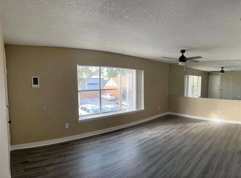 A living room with gray wood-look flooring, a large window, and a mirrored wall — 5425 HANSEL AVENUE UNIT N6, ORLANDO, FL
