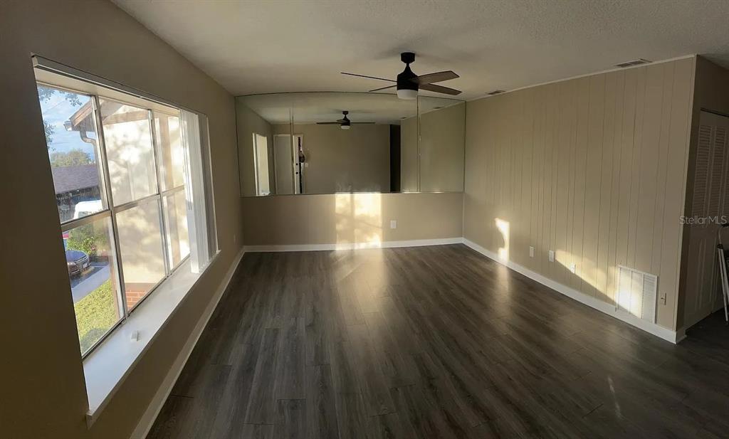 A living room with wood-look flooring, a large window, and a mirrored accent wall — 5425 HANSEL AVENUE UNIT N6, ORLANDO, FL