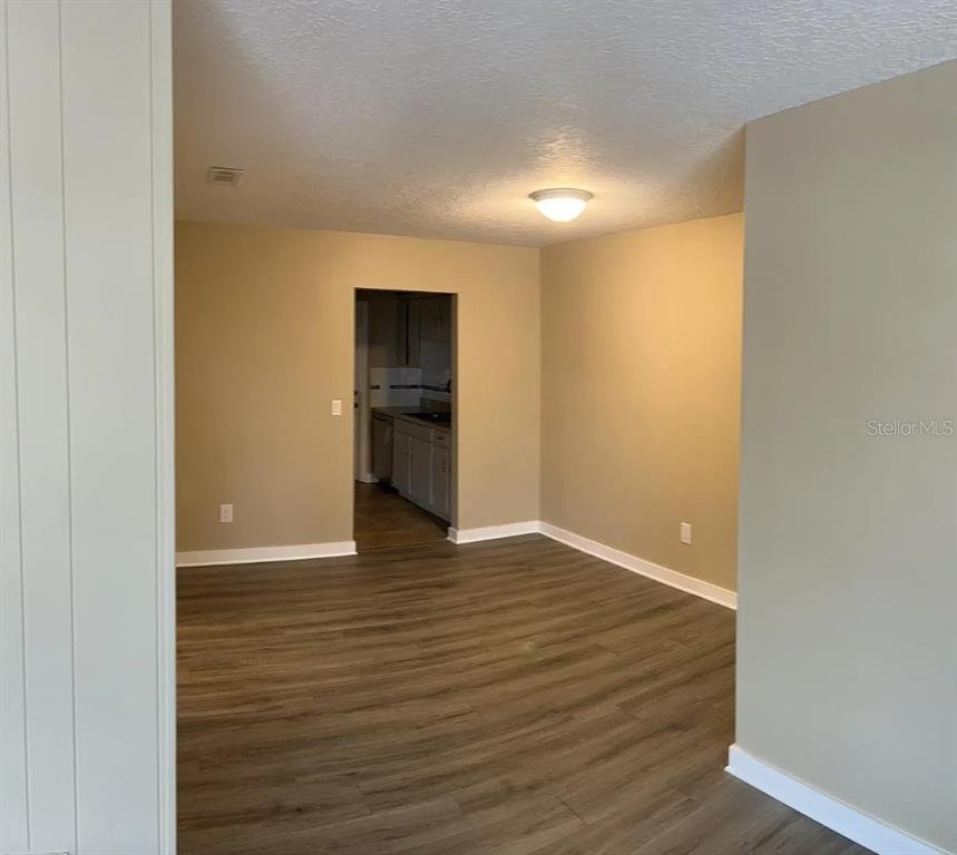 An empty room with wood-look flooring and beige walls leads to a kitchen doorway — 5425 HANSEL AVENUE UNIT N6, ORLANDO, FL