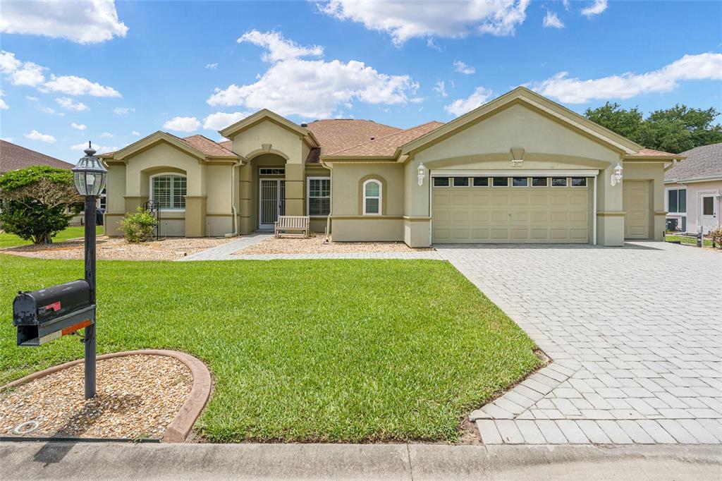 A single-story house with a beige stucco exterior, a paved driveway, and a front lawn — 13500 SE 97TH TERRACE ROAD, SUMMERFIELD, FL