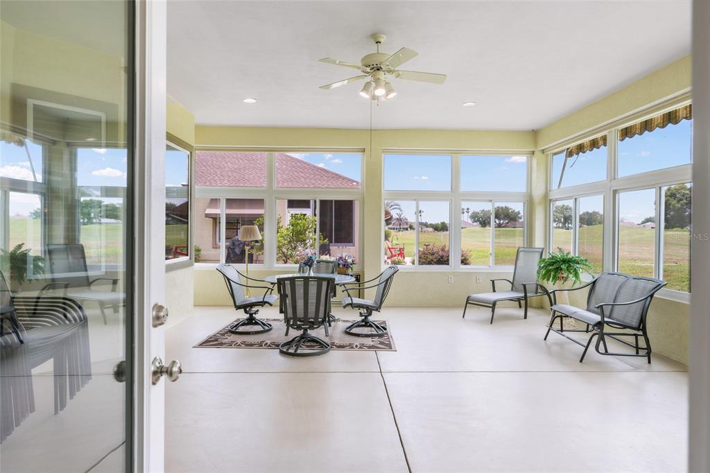 A sunroom features a dining set, lounge chairs, a ceiling fan, and large windows — 13500 SE 97TH TERRACE ROAD, SUMMERFIELD, FL
