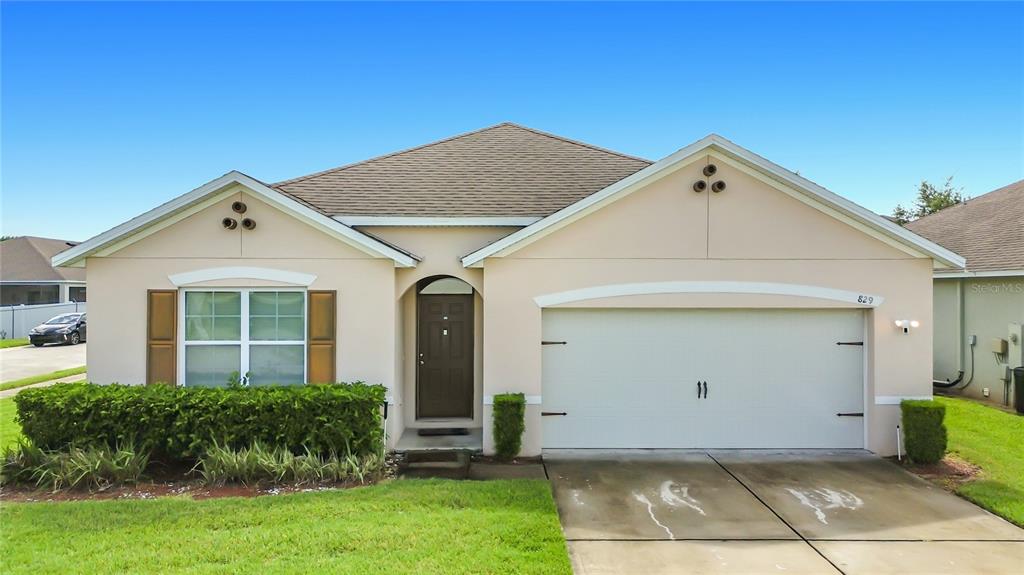A single-story house with a beige stucco exterior, a two-car garage, and a front lawn — 829 SHEEN CIRCLE, HAINES CITY, FL