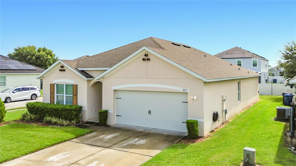 A single-story suburban house with a beige exterior, a two-car garage, and a driveway — 829 SHEEN CIRCLE, HAINES CITY, FL
