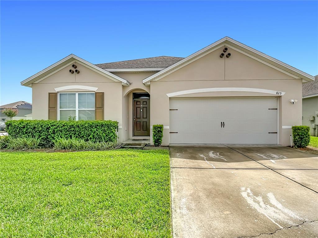A single-story beige house with a two-car garage, brown shutters, and a manicured front lawn — 829 SHEEN CIRCLE, HAINES CITY, FL