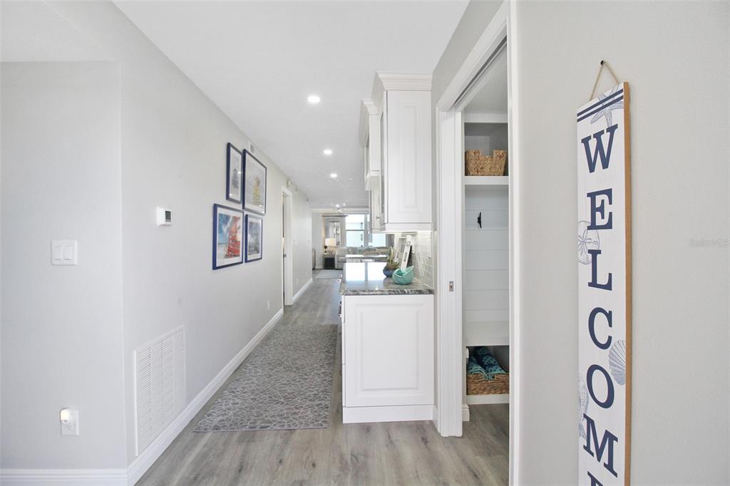 A hallway with light wood-look flooring leads past a kitchen area toward a living space — 5780 MIDNIGHT PASS ROAD UNIT 609, SARASOTA, FL