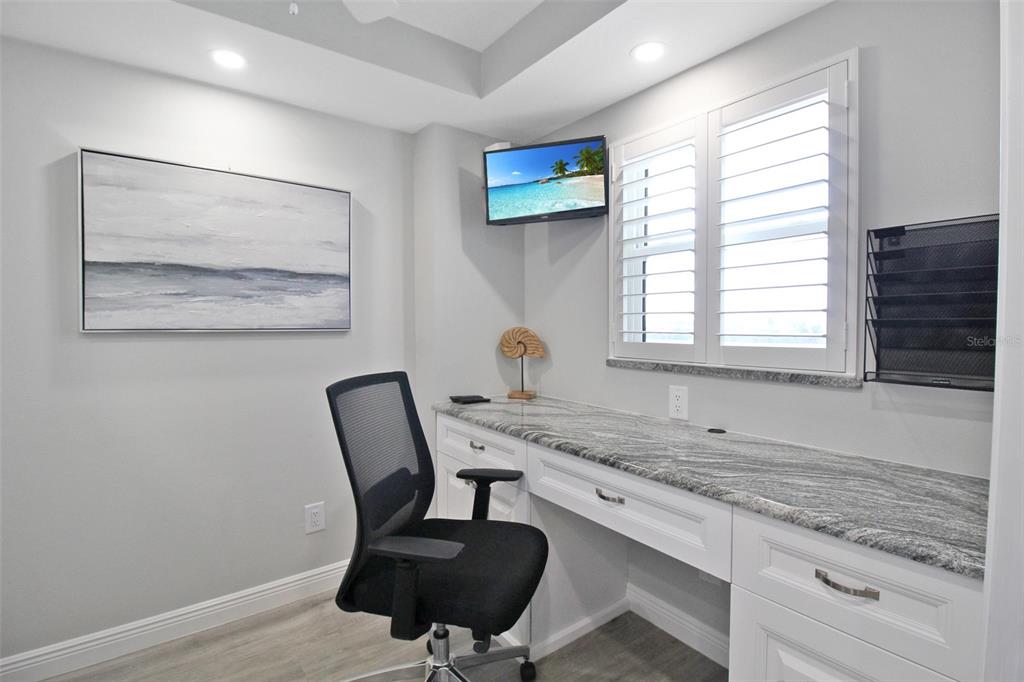 A home office features a granite desk, white cabinetry, a mesh chair, and plantation shutters — 5780 MIDNIGHT PASS ROAD UNIT 609, SARASOTA, FL