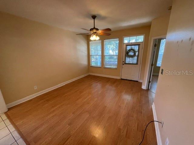 An empty room features light-colored walls, hardwood flooring, a ceiling fan, and a front door — 6344 BIRMINGHAM AVENUE, ZEPHYRHILLS, FL