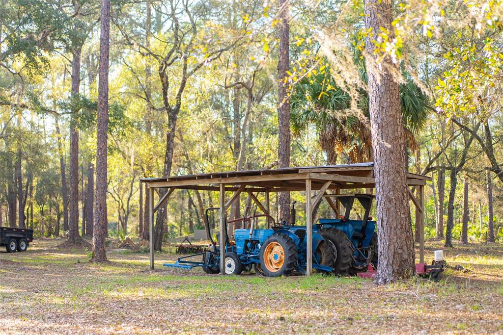 Two blue tractors are parked under a wooden shed structure in a wooded area — 8600 NE 147TH AVENUE ROAD, SILVER SPRINGS, FL