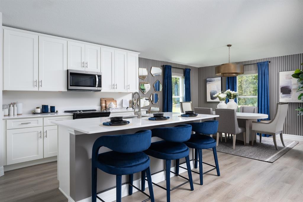 A kitchen with white cabinets, a central island with blue stools, and an adjacent dining area — 6173 SW 97TH STREET, OCALA, FL