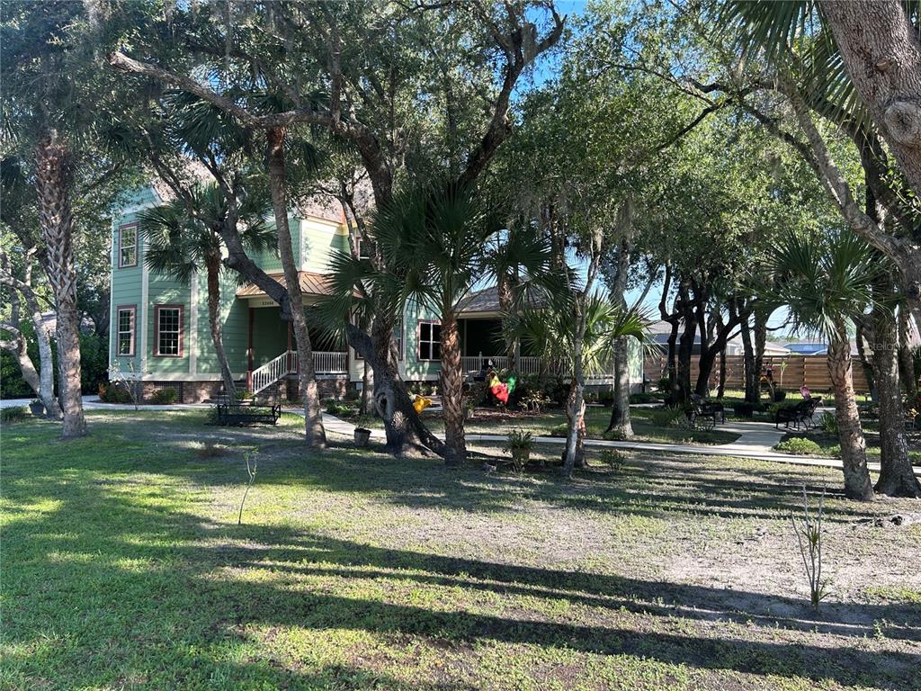 A two-story green house with a wrap-around porch sits among many trees and palm trees — 23406 AGATHA AVENUE, PUNTA GORDA, FL