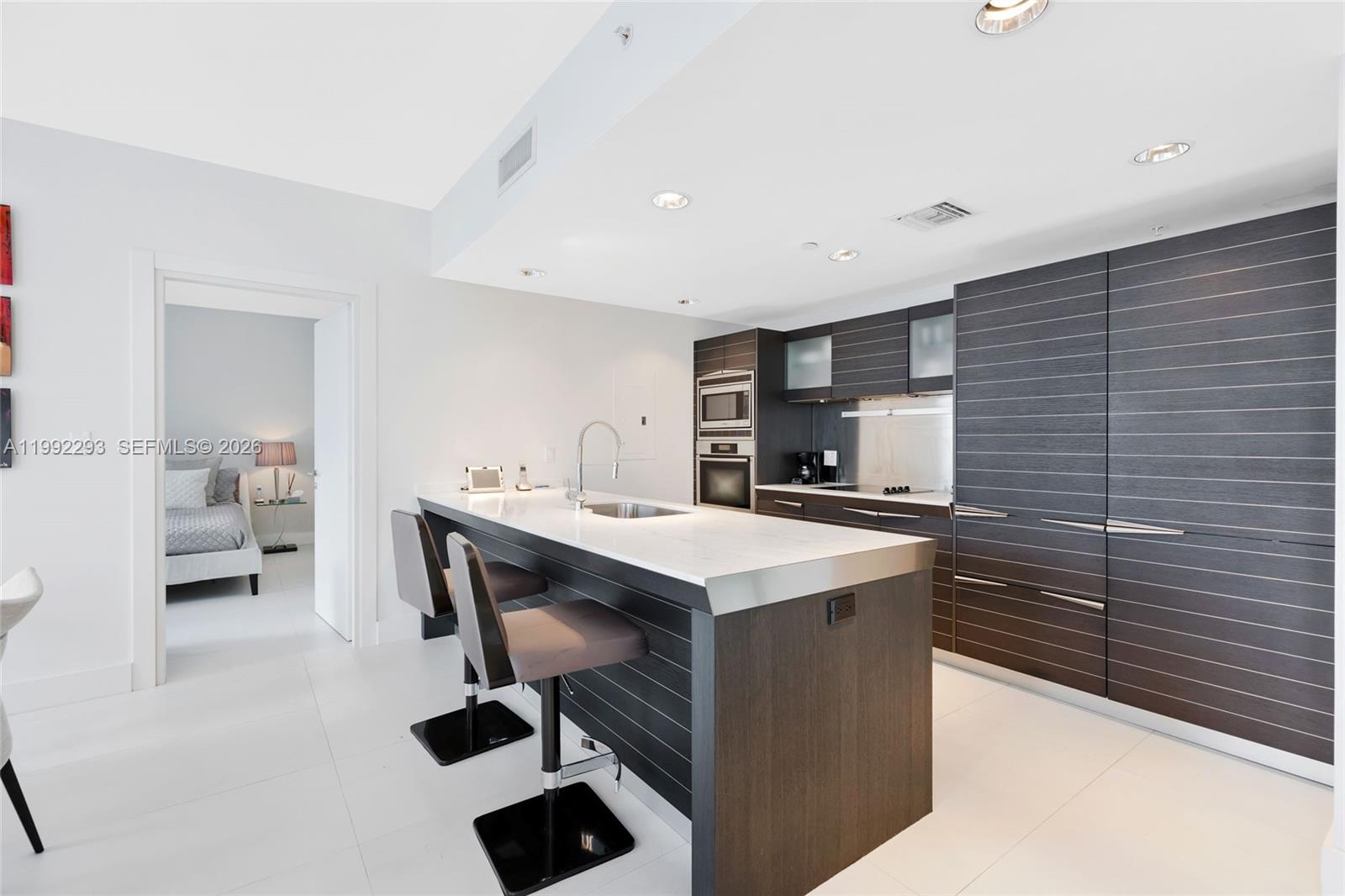 A modern kitchen features dark wood cabinetry, a white stone island, and two bar stools — 200 Biscayne Boulevard Way # 504, Miami FL 33131, MIAMI, FL
