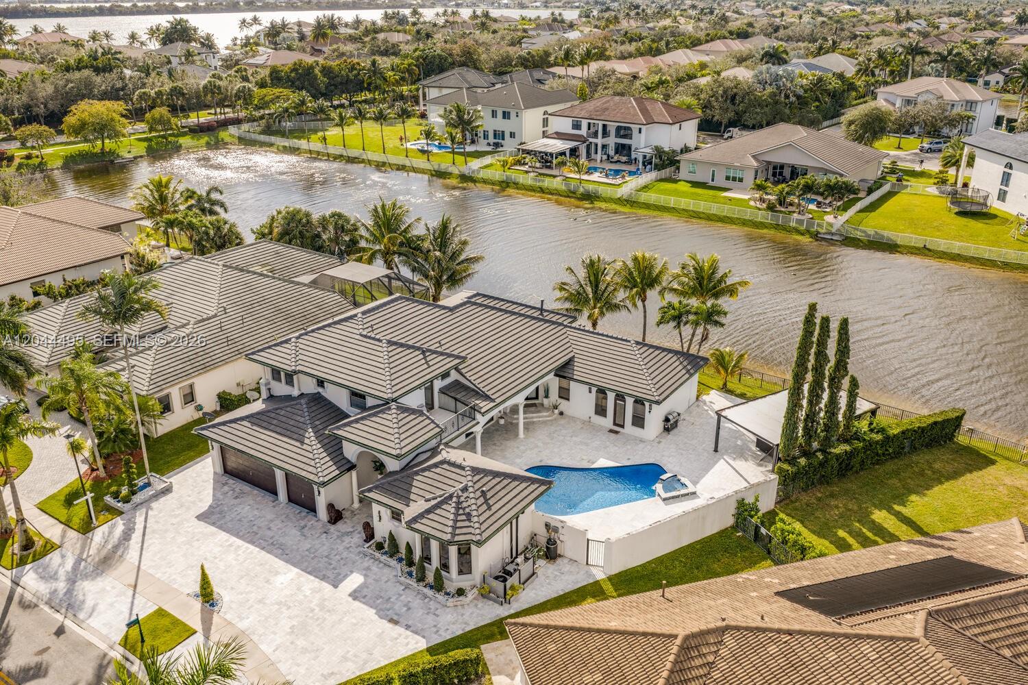 An aerial view shows a large house with a tiled roof, pool, and patio by a lake — 3910 SW 186th Ter, Miramar FL 33029, MIRAMAR, FL