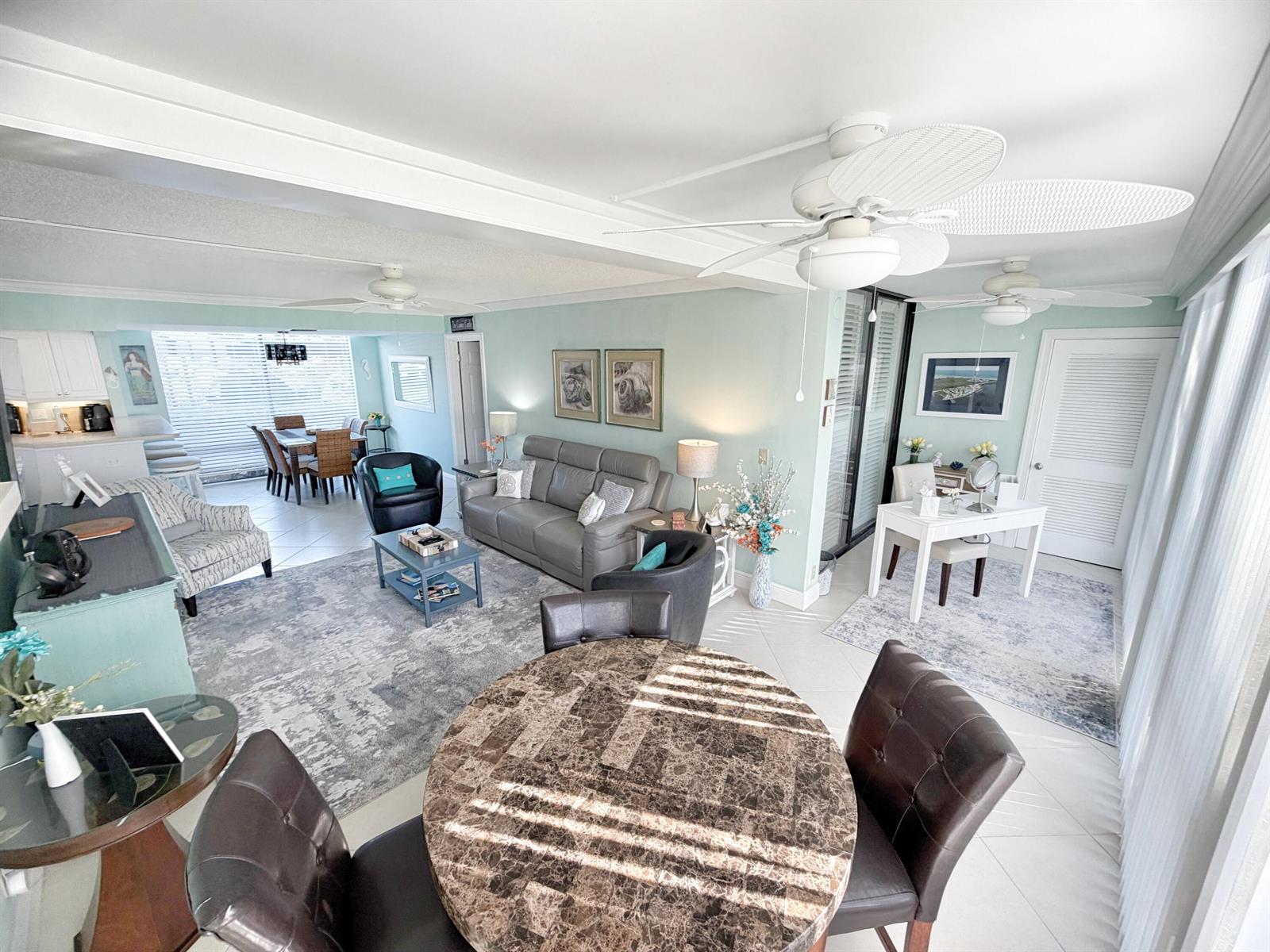 An open-concept living and dining area features light blue walls, tile floors, and ceiling fans — 3492 NE Causeway Boulevard # 101, Jensen Beach FL 34957, JENSEN BEACH, FL