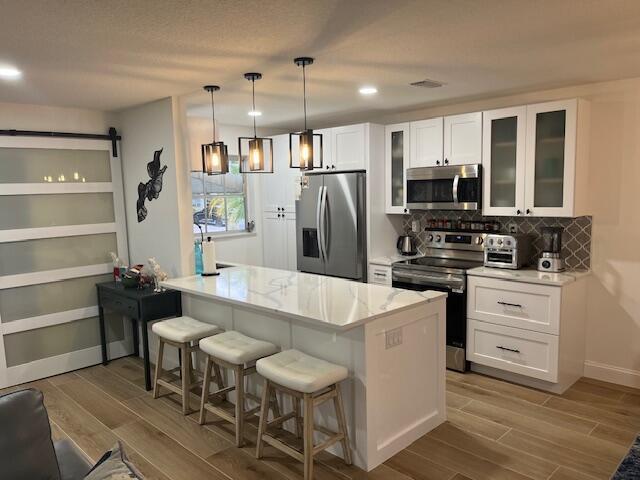 A modern kitchen features white cabinetry, a marble-topped island with stools, and stainless steel appliances — 1157 S Drive Circle # C, Delray Beach FL 33445, DELRAY BEACH, FL