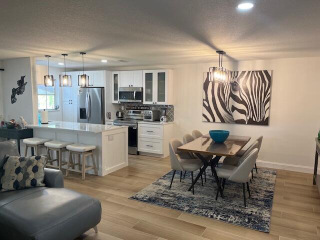 An open-concept kitchen and dining area features white cabinetry, stainless steel appliances, and zebra artwork — 1157 S Drive Circle # C, Delray Beach FL 33445, DELRAY BEACH, FL