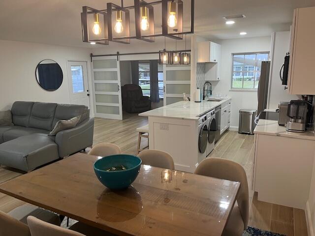 An open-concept living and dining area features a kitchen island, pendant lighting, and sliding doors — 1157 S Drive Circle # C, Delray Beach FL 33445, DELRAY BEACH, FL